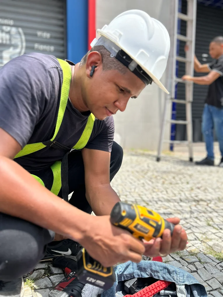 Técnico da GamaFortes instalando comunicação visual em obra, com capacete e furadeira